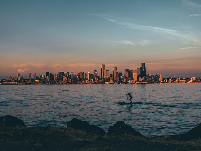 Paddleboarder off the shore of Alki beach with the cityscape of Seattle in the background at sunset
