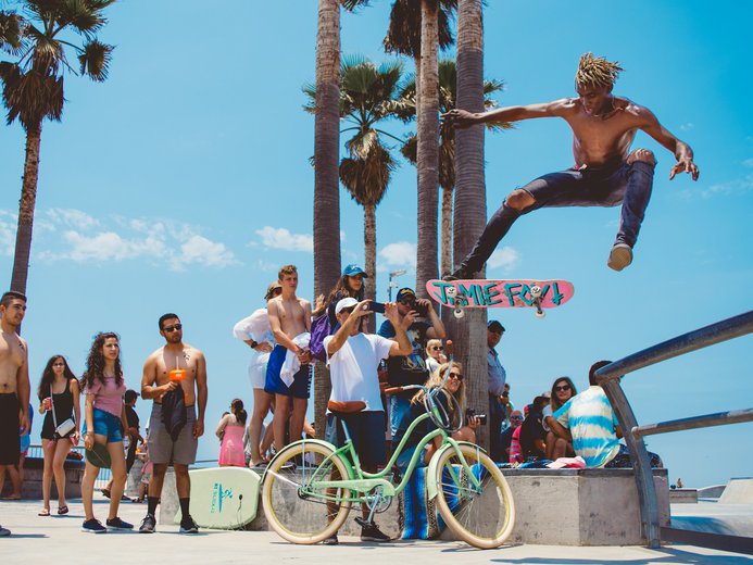 Skateboarder doing a trick in the air with lots of people watching at Venice Beach in California