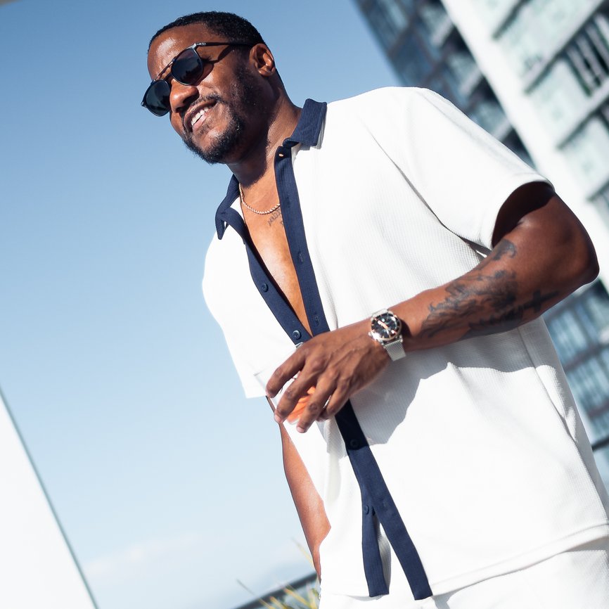 man standing outside in the sun on balcony with a drink in hand